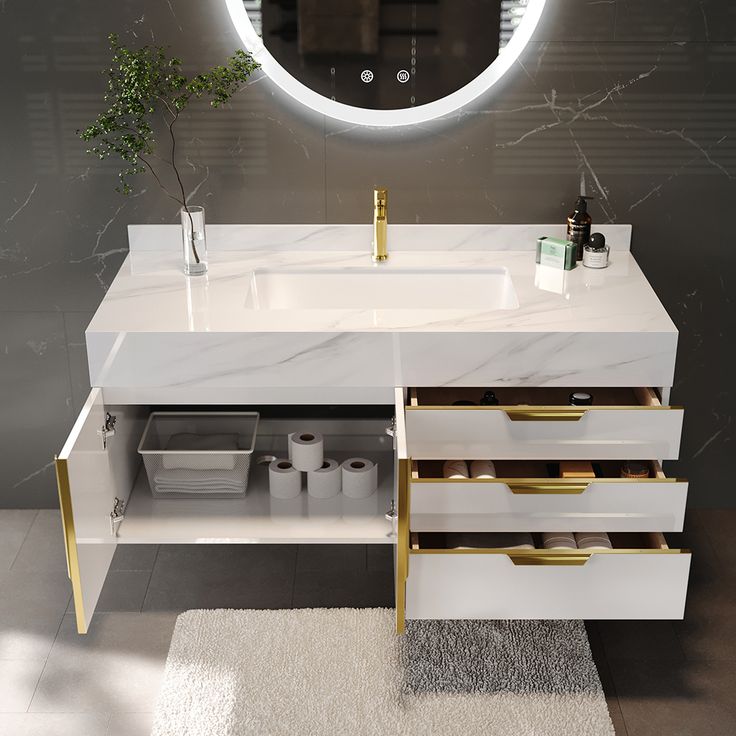 a bathroom vanity with marble counter top and gold accents on the drawers, under a round mirror