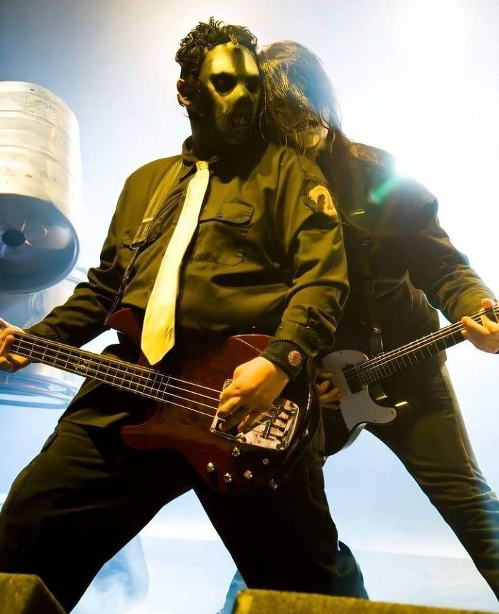 two men in masks are playing bass guitars and one is wearing a yellow neck tie