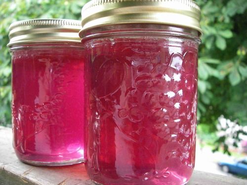 three jars filled with pink liquid sitting on top of a wooden table next to trees