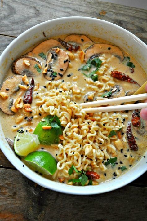 someone holding chopsticks over a bowl of noodles with mushrooms, peppers and broccoli