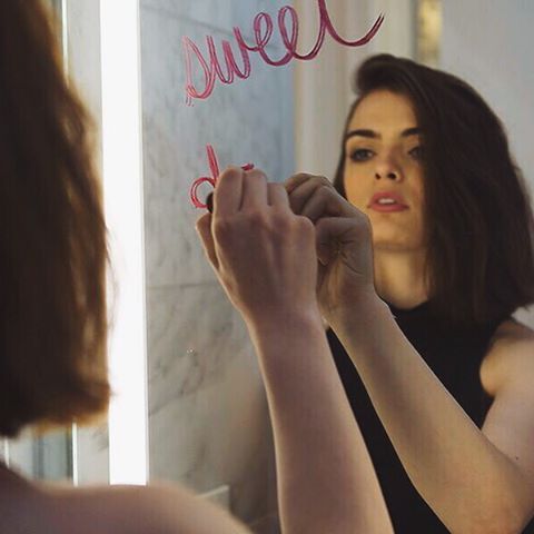 a woman is writing on the mirror with pink letters in front of her and she is looking at herself