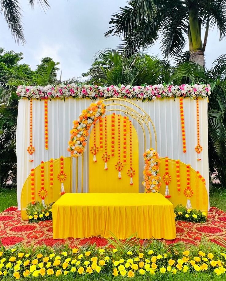 a yellow and white stage set up with flowers on the side, decorated with orange and pink garlands