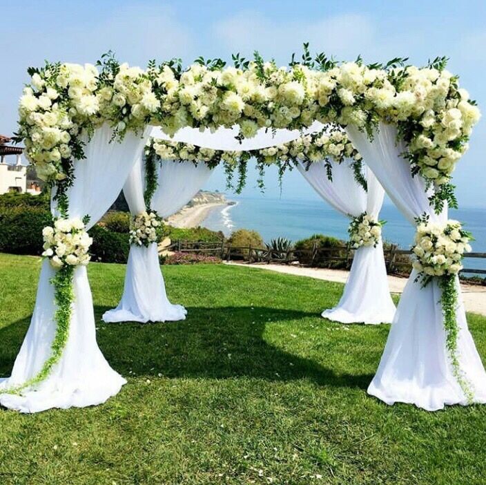 an outdoor wedding ceremony setup with white flowers and greenery on the grass by the ocean