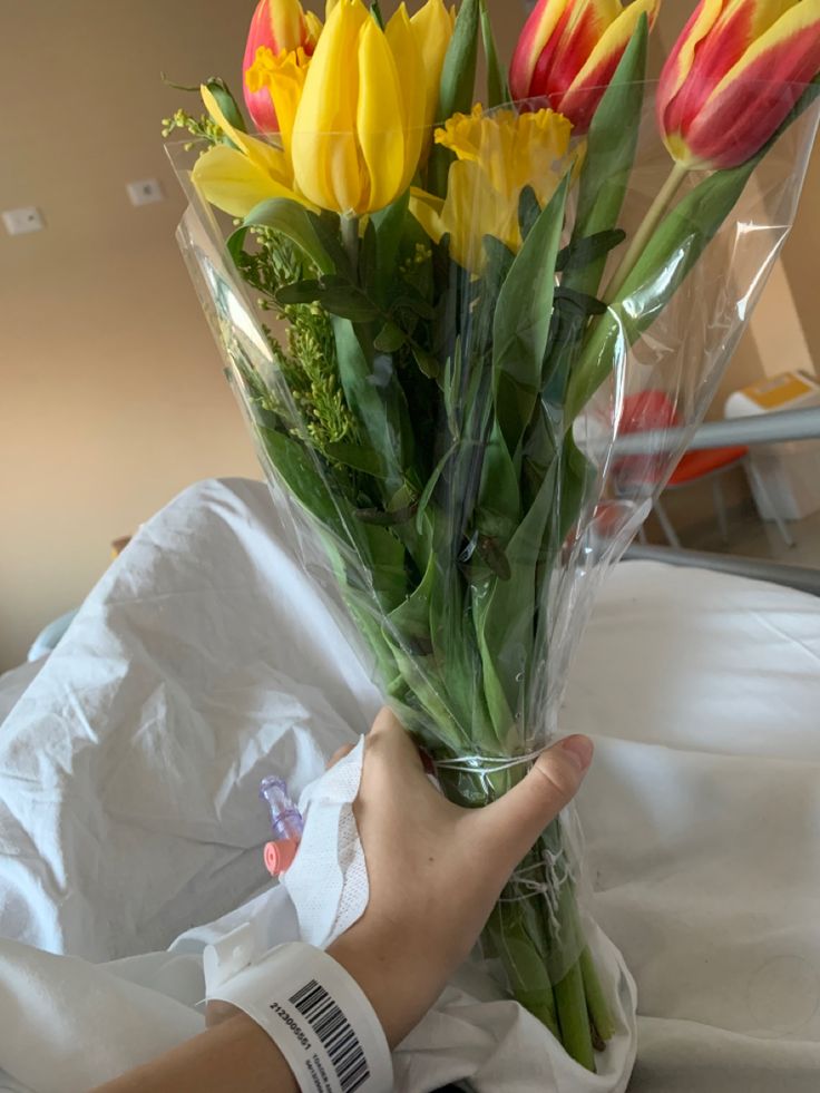 a person holding a bouquet of flowers on top of a white sheet covered bed in a room