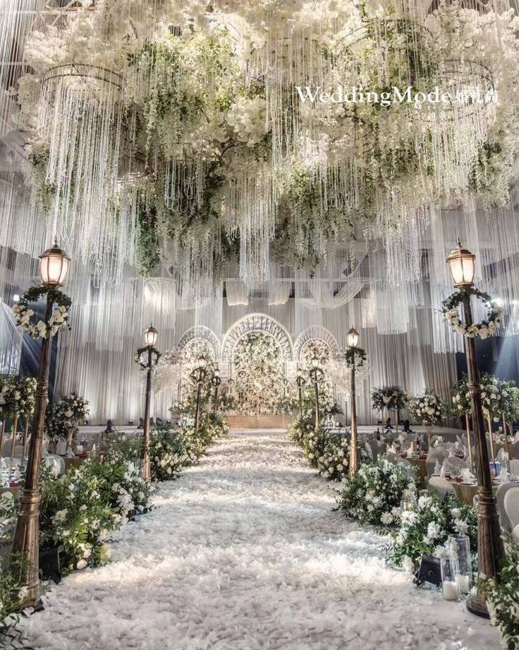 an elaborate wedding ceremony setup with chandeliers and white flowers on the ceiling, surrounded by greenery