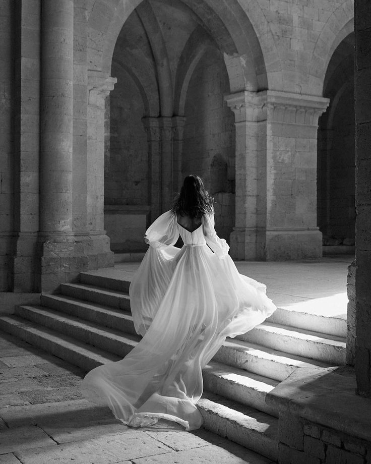 a woman in a long white dress is walking up some stairs