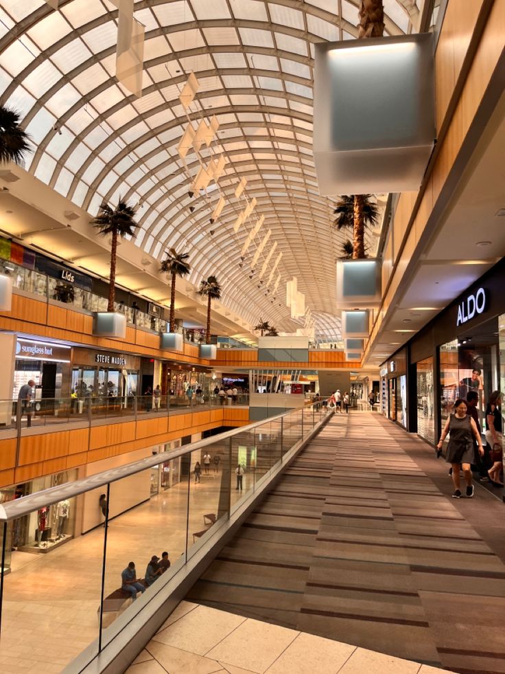 the inside of a shopping mall with people walking around and palm trees hanging from the ceiling