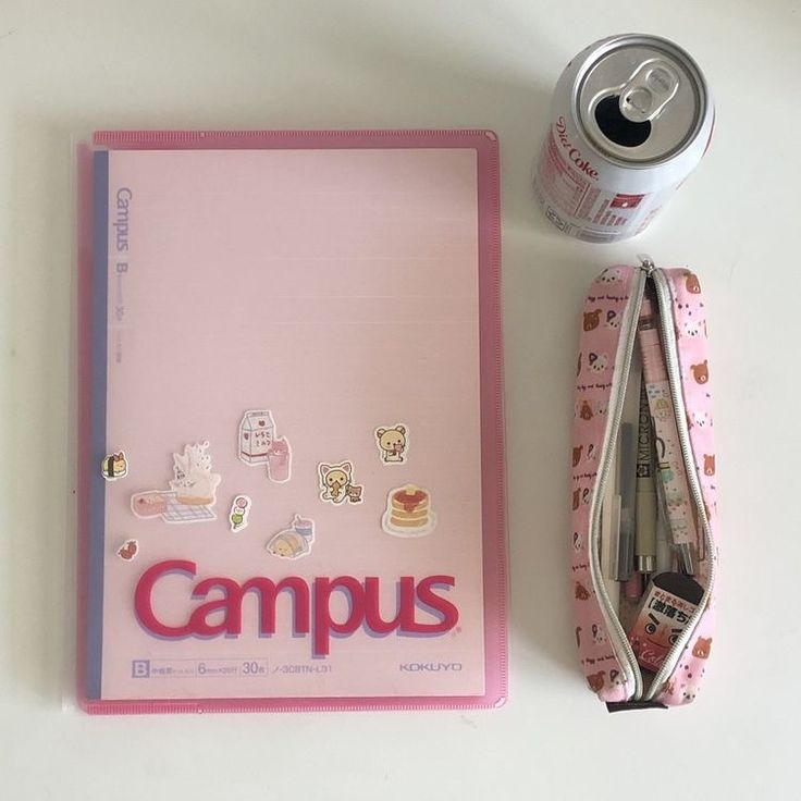 a pink notebook with some stickers on it next to a can of soda