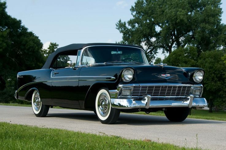 an old black car is parked on the side of the road in front of some trees