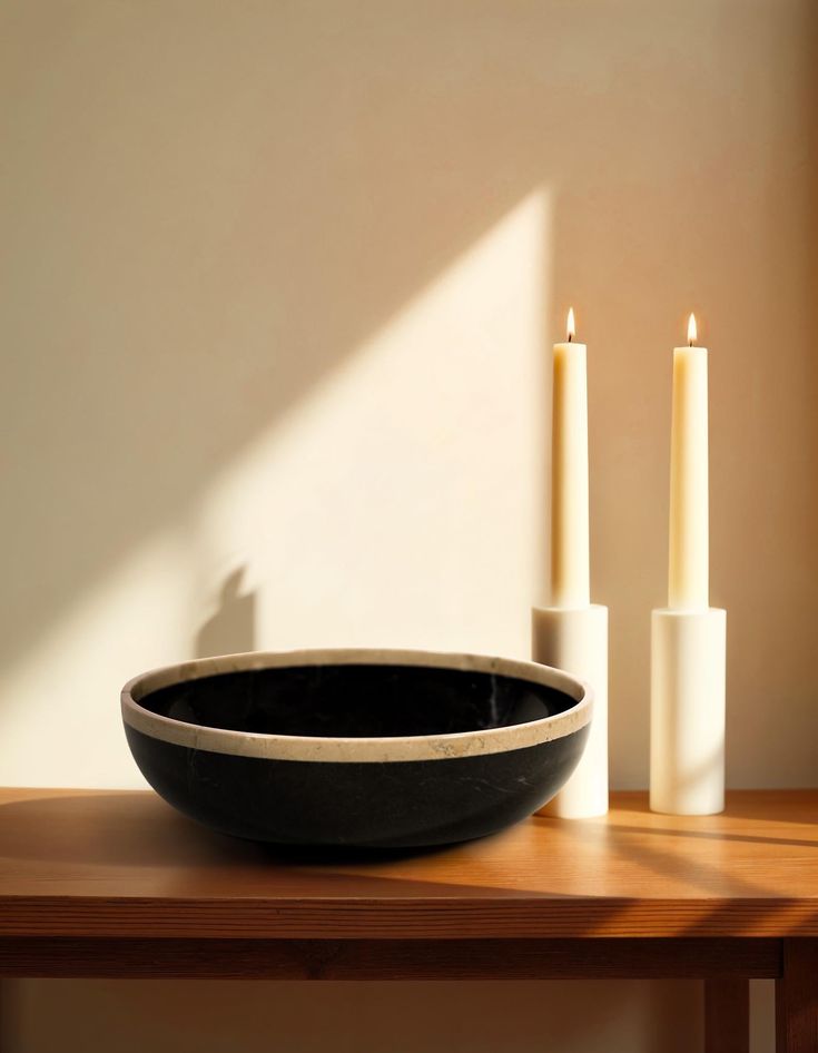 a black bowl sitting on top of a wooden table next to two white candle holders