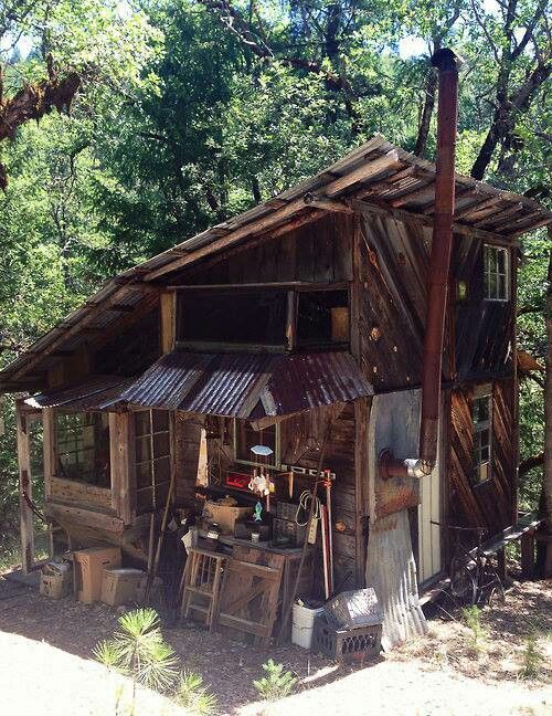 an old wooden shack with lots of junk on the ground and trees in the background