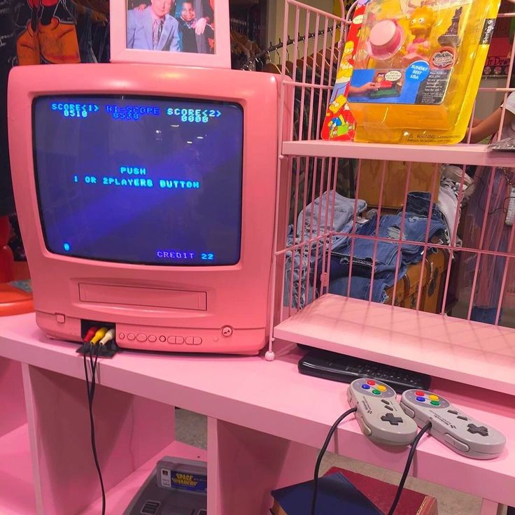 a pink computer monitor sitting on top of a desk next to a video game controller