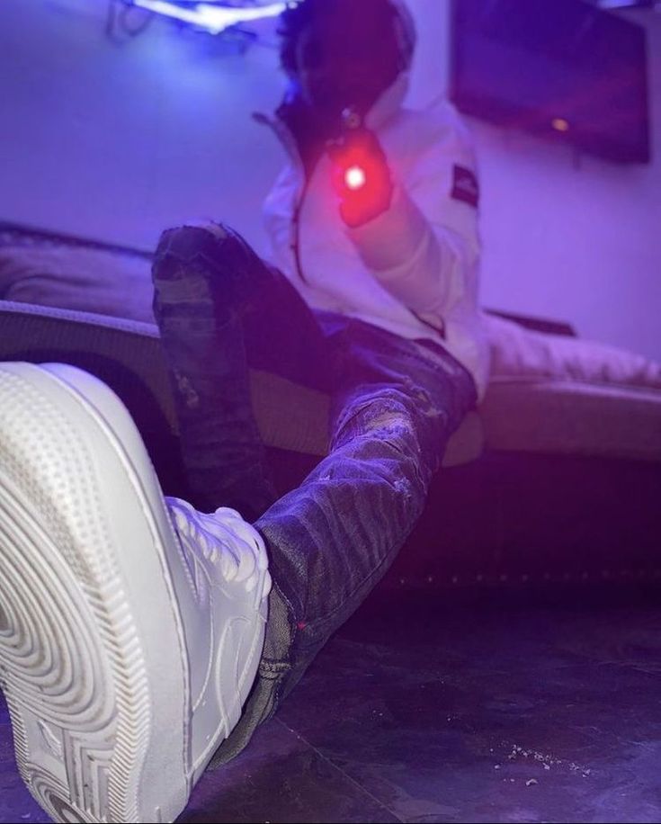 a person sitting on a bed with their feet up in the air while wearing white sneakers