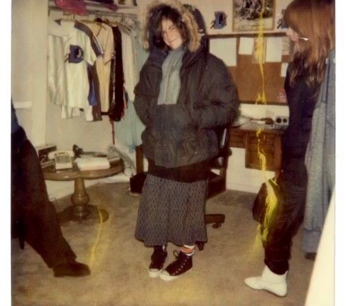 two women are standing in a room with clothes on the walls and one is wearing a fur hat