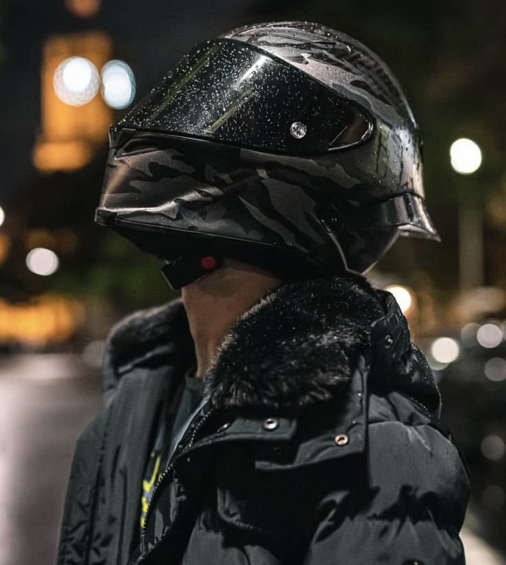 a person wearing a helmet and jacket on the street at night with buildings in the background