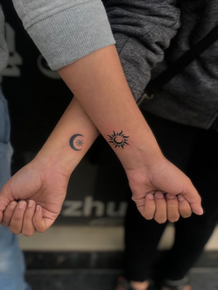 two people are holding hands with tattoos on their arms and one has a sun and moon