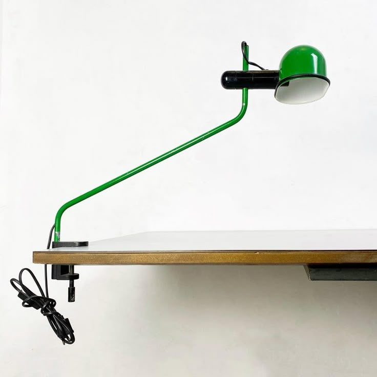 a green lamp on top of a wooden table next to a white wall and black cord