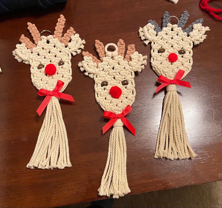 three crocheted reindeer ornaments with red bows on them sitting on a wooden table