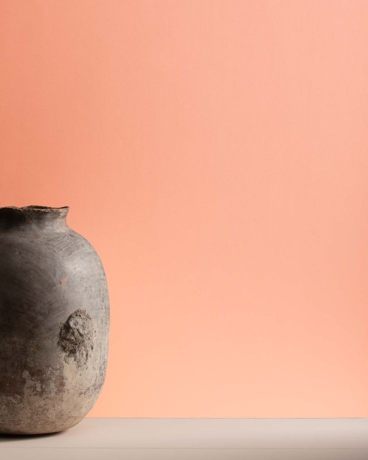 a black vase sitting on top of a table next to a pink wall in the background