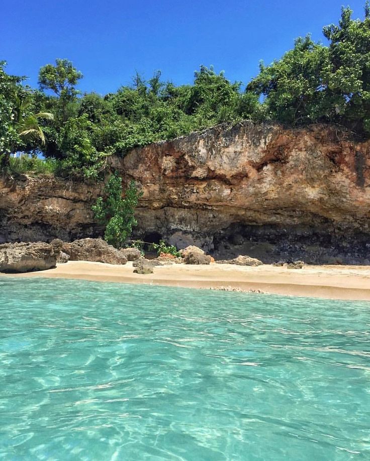 the water is crystal blue and clear, with trees on the cliff in the background