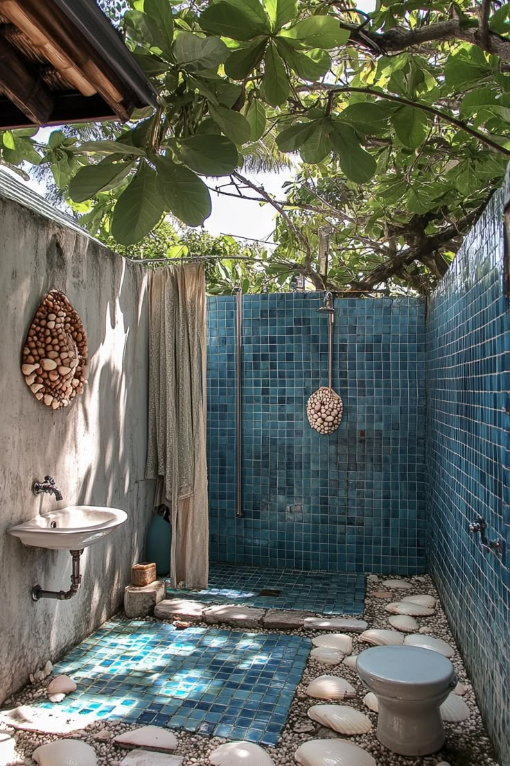 a bathroom with blue tile and stone flooring next to a tree in the shade