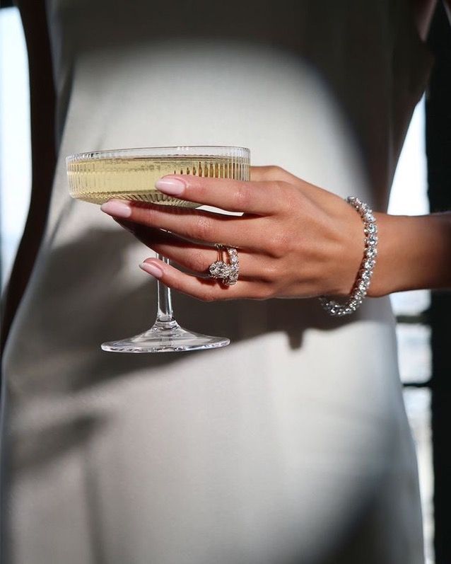 a woman's hand holding a champagne glass in front of her belly and wearing a diamond bracelet