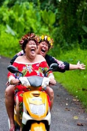 two people riding on the back of a yellow scooter in front of trees