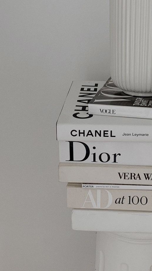 three books stacked on top of each other in front of a white vase and wall