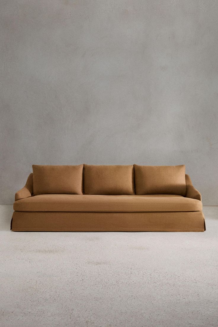 a tan couch sitting on top of a white floor next to a gray wall with two pillows