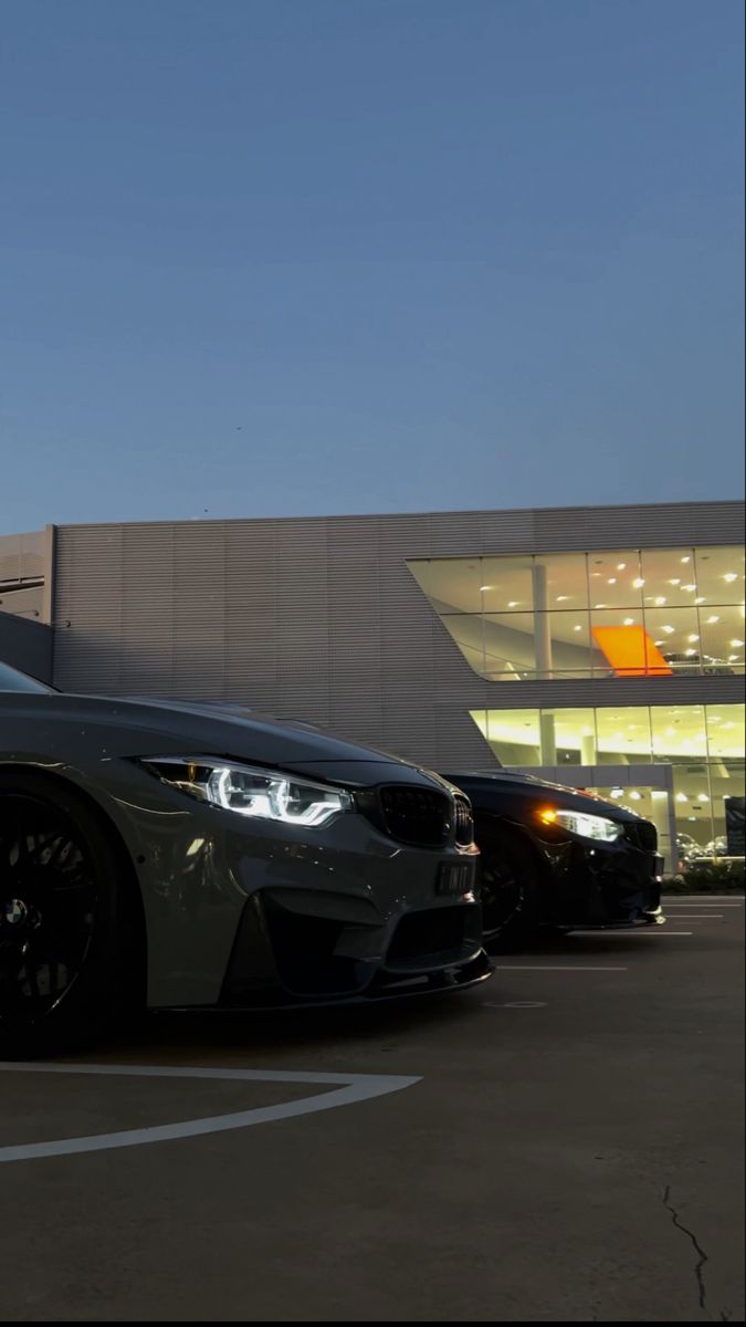 two bmw cars parked in front of a building at night with lights on the windows