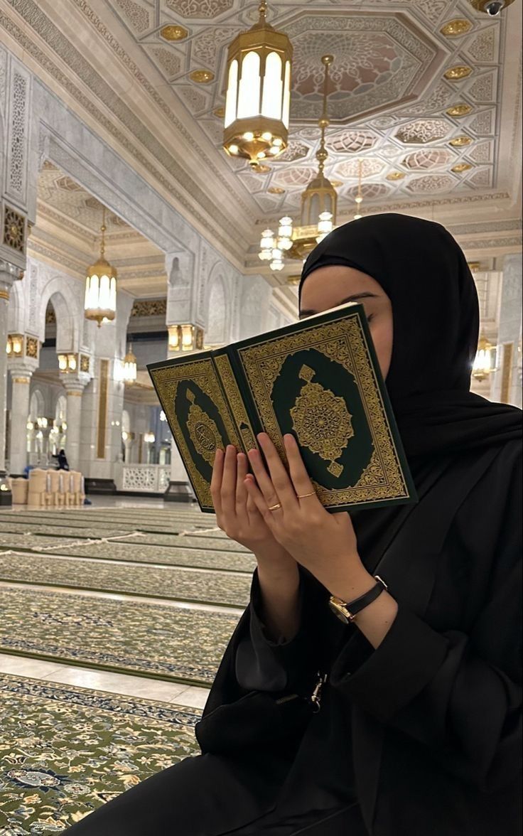 a woman wearing a black hijab is holding a book in front of her face