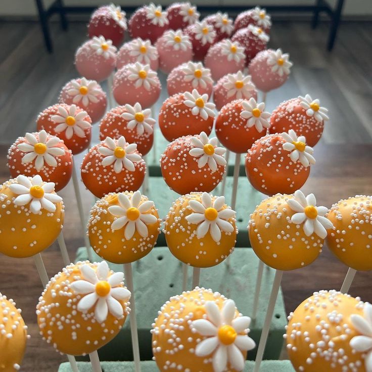 there are many cake pops with daisies on them in the box and one is orange