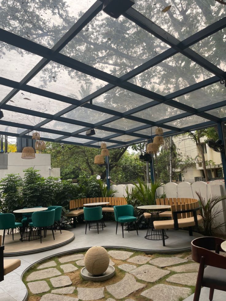 an outdoor dining area with tables and chairs under a pergolated roof, surrounded by greenery