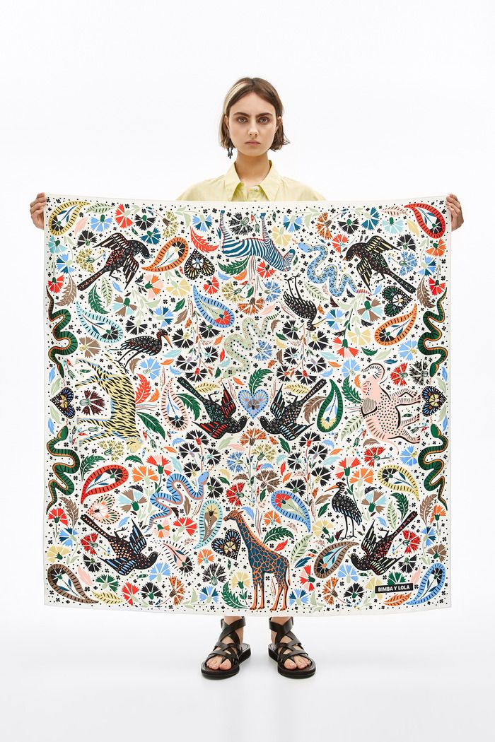 a woman holding up a large tapestry with animals and flowers all over it's surface