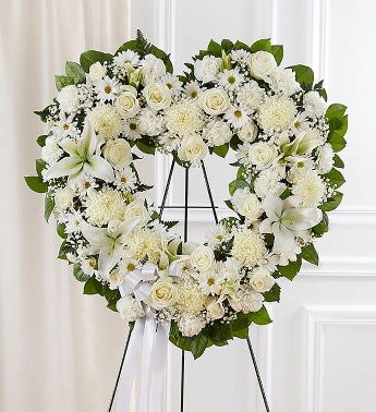 a heart shaped wreath with white flowers and greenery