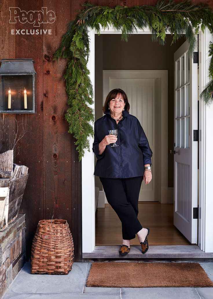 a woman standing in front of a door holding a coffee cup and smiling at the camera