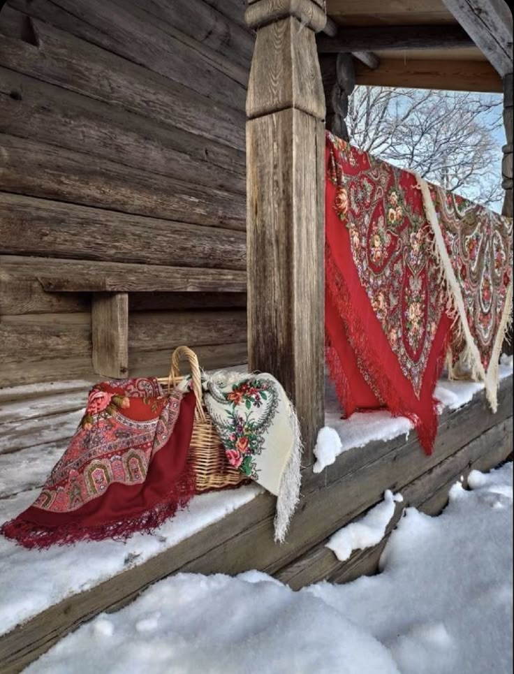 some blankets are hanging on the side of a wooden structure in the snow near a log cabin