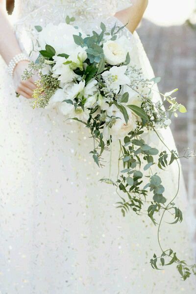 a woman in a wedding dress holding a bouquet of white flowers and greenery on her arm