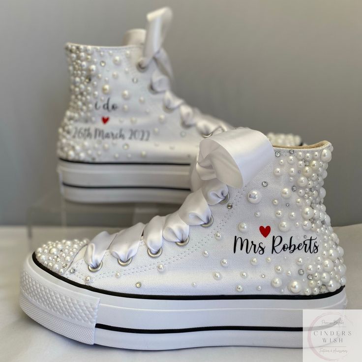 a pair of white high top sneakers with pearls and hearts on the side, decorated with personalized names