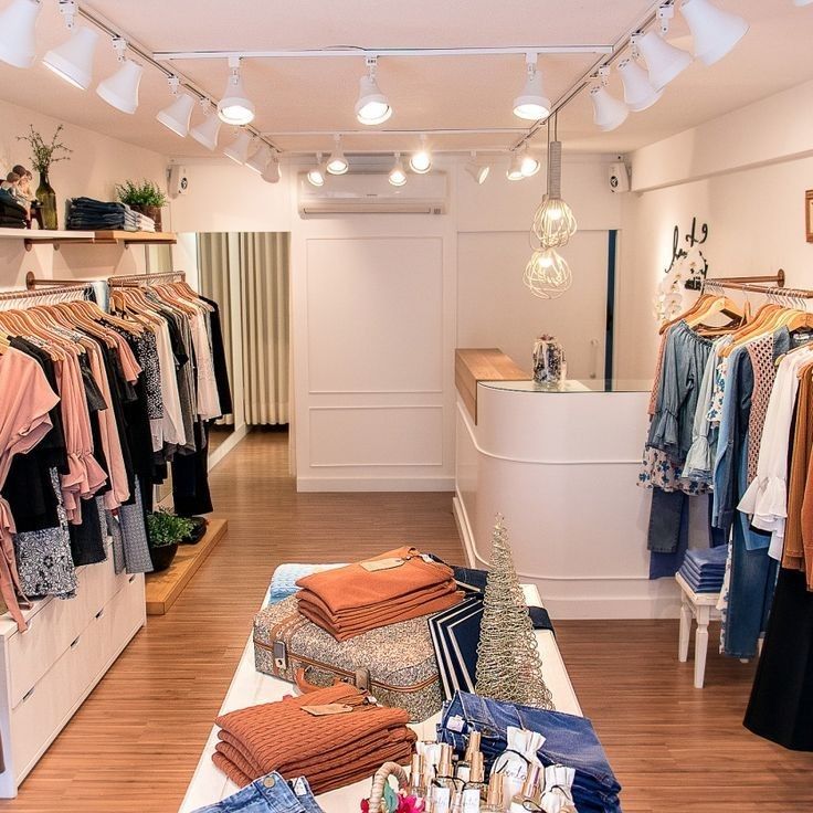 the inside of a clothing store with lots of clothes on racks and lights hanging from the ceiling