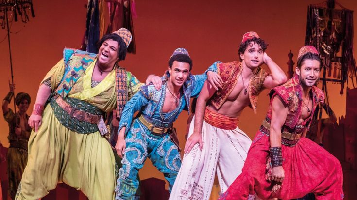 men and women in colorful costumes on stage with one man holding his arm around the other