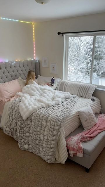 a woman laying in bed next to a window with pink and white blankets on it