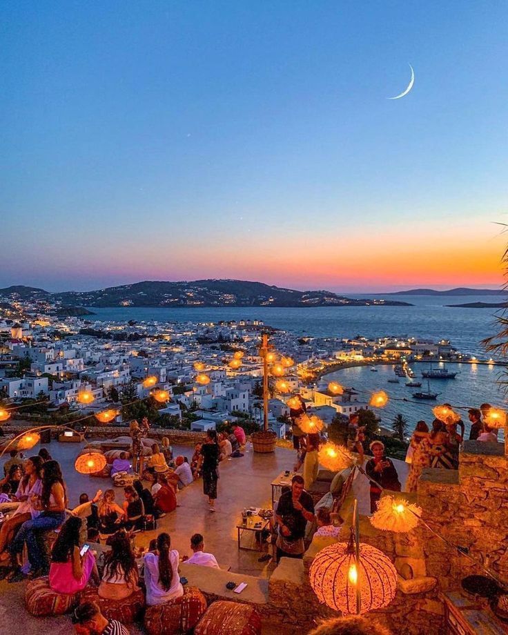 many people are sitting on the beach at night with lanterns in the sky and water