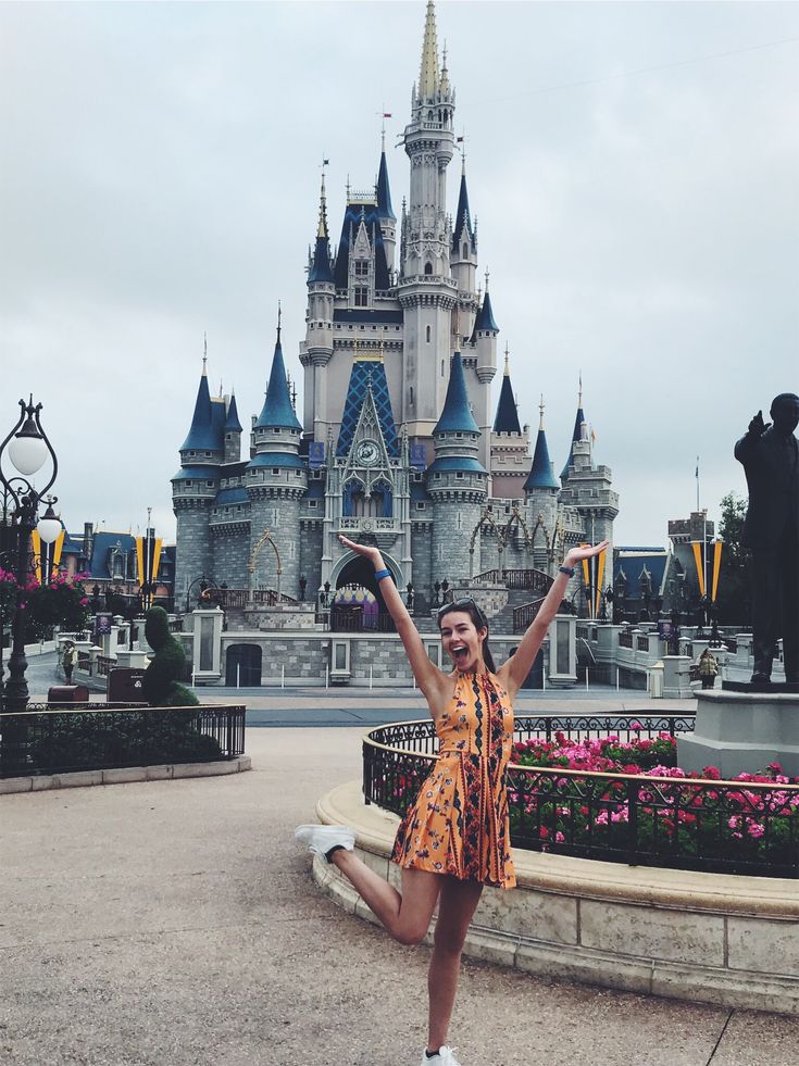 a woman standing in front of a castle with her arms up and hands raised above her head