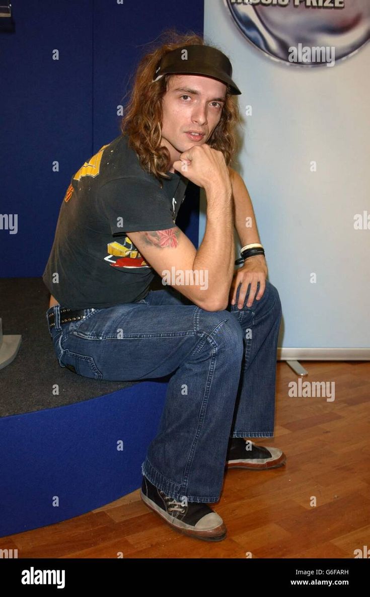 a man with long hair sitting on the floor in front of a blue wall and posing for