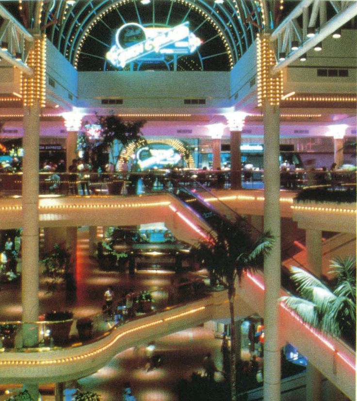 the inside of a shopping mall with lights and palm trees in the foreground at night