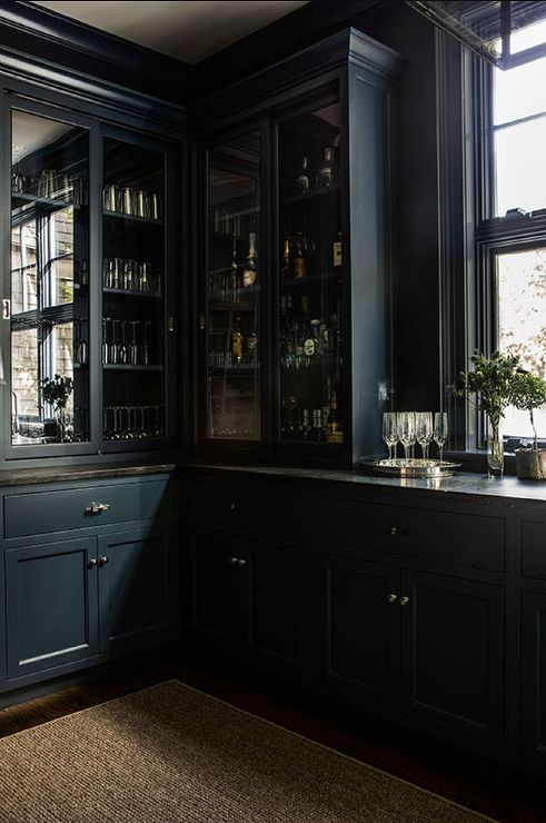 an empty kitchen with black cabinets and glassware on the counter top, in front of a large window