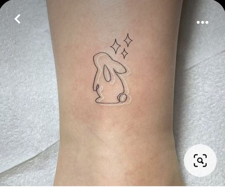 a small tattoo on the ankle of a woman's left leg, with an outline of a dog and stars above it