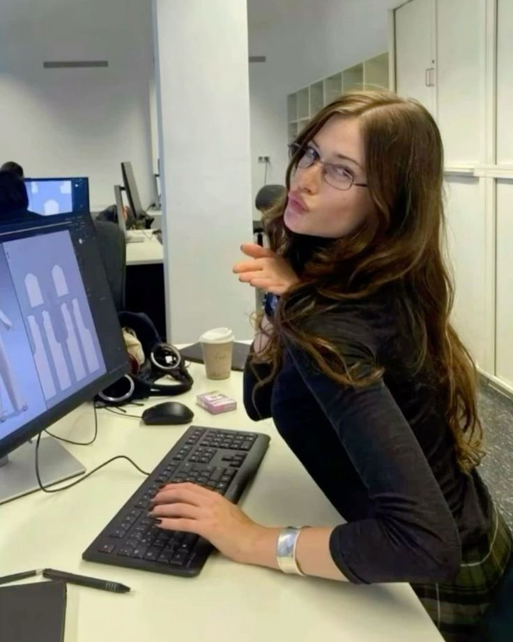 a woman sitting at a desk with a computer monitor and keyboard in front of her