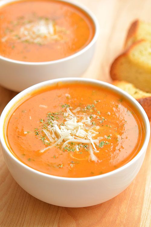 two bowls of tomato soup with parmesan cheese on top and bread slices in the background